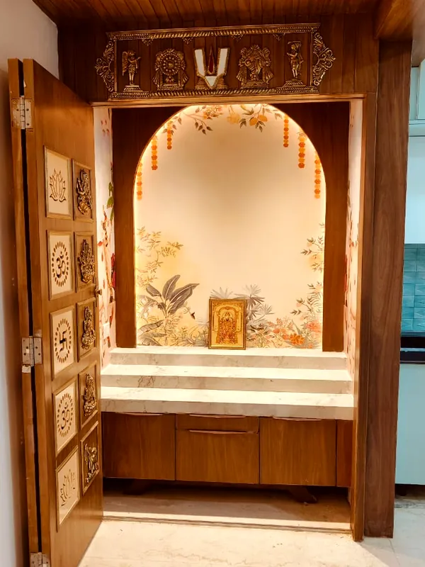 A pooja room under an arch, behind carved doors.